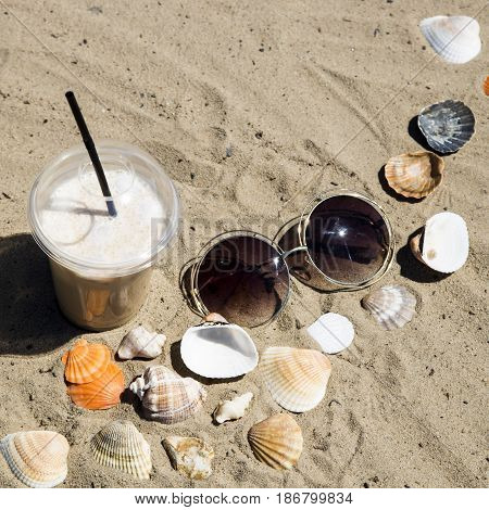 Ice latte on sand with cockleshells and glasses