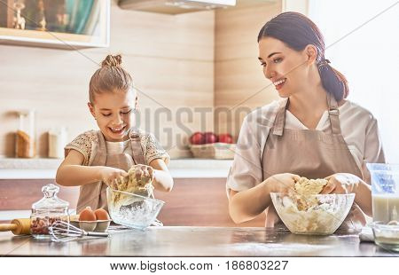 Happy loving family are preparing bakery together. Mother and child daughter girl are cooking cookies and having fun in the kitchen. Homemade food and little helper.