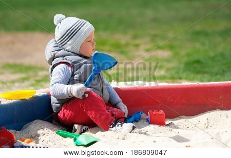 Portrait of toddler child wearing vest jacket outdoors. One year old baby boy playing with sand at playground sandbox
