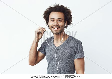 Happy african man putting out headphone lookig at camera smiling. White background. Copy space.