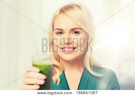 healthy eating, vegetarian food, diet, detox and people concept - smiling young woman drinking green vegetable juice or smoothie from glass at home