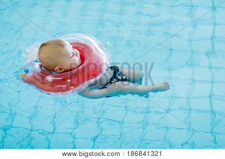 Cute little baby child learning to swim with swimming ring in an indoor pool. 