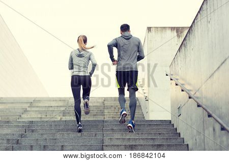 fitness, sport, people, exercising and lifestyle concept - couple running upstairs on city stairs