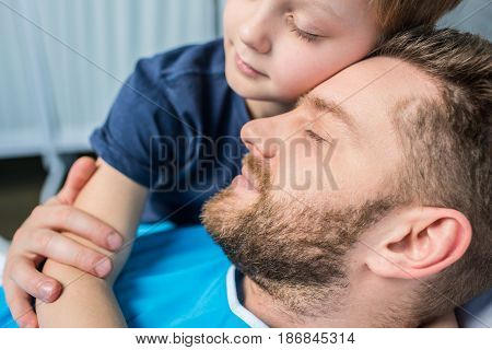 Father With Son Embracing While Laying On Hospital Bed At Ward, Dad And Son