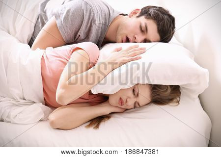 Young irritated woman lying in bed with snoring husband at home