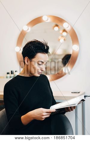 Attractive woman primp at the mirror with lamps in the beauty studio. A happy satisfied customer of make-up and hairstyle service.