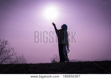 Silhouette Muslim Arabic woman praying with her hands up