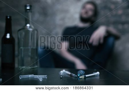 Blurred poisoned reality. Used medical unpacked syringes lying on the table while freak sitting in the background