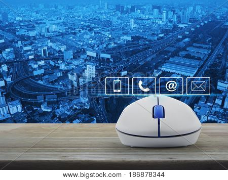 Telephone mobile phone at and email buttons with wireless computer mouse on wooden table over city tower street and expressway Customer support concept