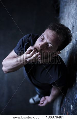 Enjoying my accelerated heartbeat. Freaked young bearded junkie holding marijuana cigarette while smoking and expressing indifference to everything