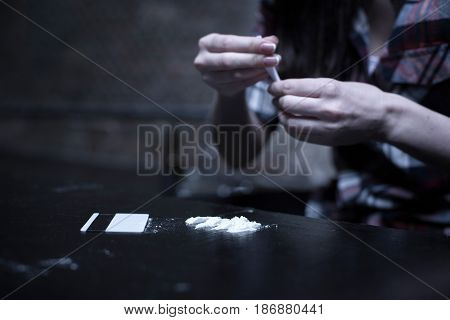 Preparing dose of heroin . Apathetic desperate young woman sitting in the dark place while preparing heroin lines and holding drug