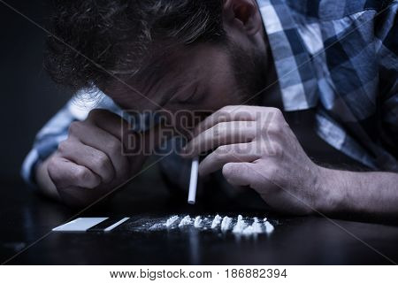 Spending every day on the edge . Depressed young bearded freak sitting in the dark room while snorting heroin lines and getting new drug dose