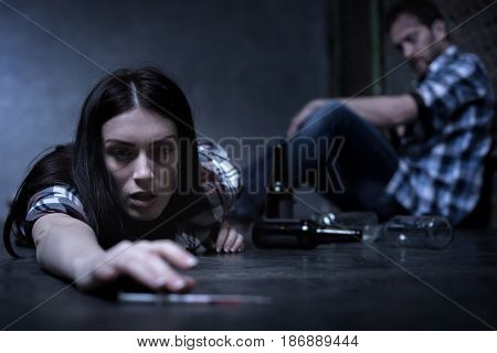 Lethal reaction to drug. Horrible overdosed exhausted woman lying on the ground at the opium den and suffering from big heroine dose while other addict siting in the background