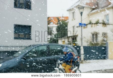 Silhouette of child kid on bike crossing street on a snowy day - senn by the driver point ov view personal perspective through wet windshield window