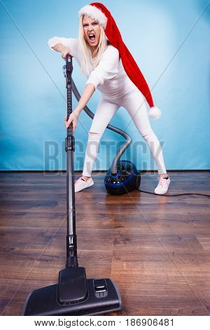 Woman vacuuming the house last minute. Teen girl in santa helper hat with vacuum cleaner angry furious face expression. Christmas time and housework concept.