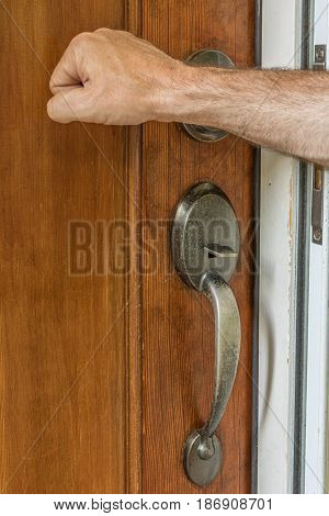 Male hand knocking on a wooden door with door handle in the shot