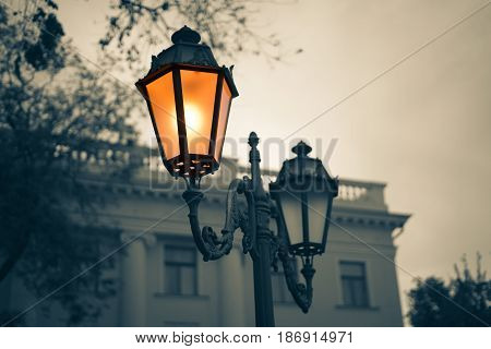 Black and white picture of Old Vintage street light with old building on background. Lamp light is colored.
