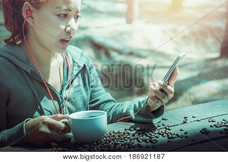 Women drink coffee Play mobile phone On the wooden table floor there is a coffee bean.