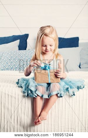 Cute Child Girl Opening Gift with Blue Ribbon at Home. Child with Gift Box