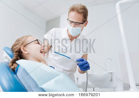 Contemporary technologies. Competent friendly scrupulous doctor conducting a procedure employing some tools while treating his patients teeth