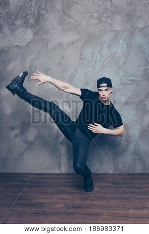 Handsome Young Break Dancer Is Making His Favourite Move In Studio On The Grey Background. He Is Wea