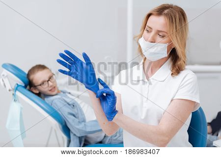 Professional preparations. Focused competent scrupulous doctor using special gloves for protecting herself and her patient from any infections and getting ready performing a procedure