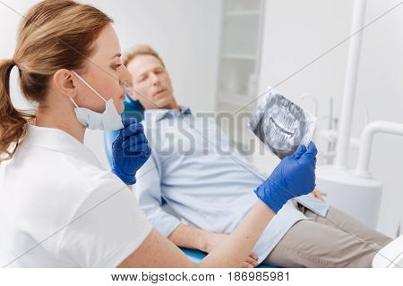 It will take some effort. Distinguished clever focused doctor examining patients jaw scan and analyzing the results while developing a plan of his treatment