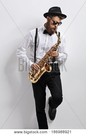 Jazz musician leaning against a white wall and playing saxophone