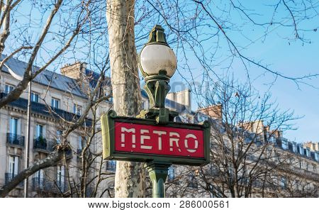 Paris, France, February 13, 2019: A Traditional Red Metro Sign In Winter With Haussmann Buildings In