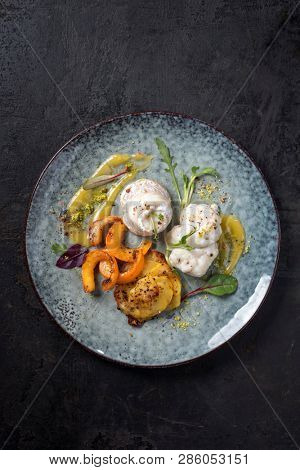 Fried Norwegian skrei cod fish filet with potatoes, pumpkin and lemon curd as top view on a modern design plate 
