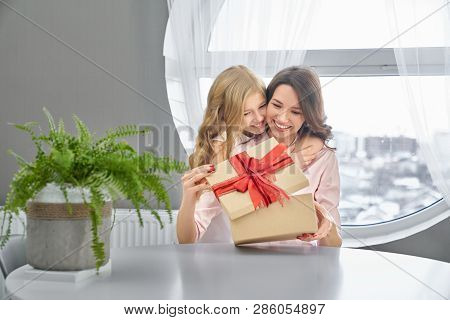 Daughter Congratulating, Giving To Mom Surprise On Mothers Day. Beautiful Girl With Long, Curly Hair