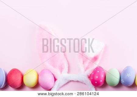 Easter Rabbit Flaffy Ears And Row Of Colored Easter Colored Eggs On Pink Background, Top View With C