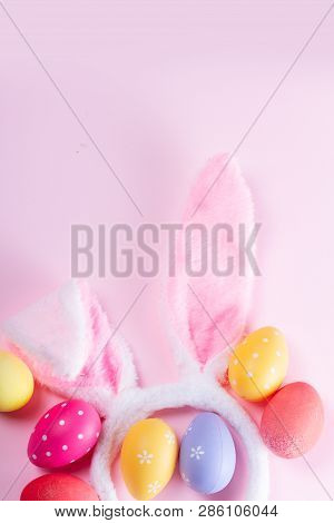 Easter Rabbit Flaffy Ears And Colored Easter Colored Eggs On Pink Background, Flat Lay With Copy Spa