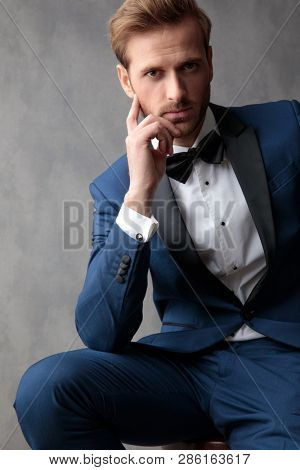 Elegant man  seating on a chair, holdiing a hand at his chin, thinking about something while looking at the camera