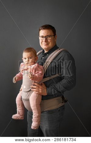 Fathre And His Kid In Baby Carrier At The Grey Background Wall, Baby Wearing Concept