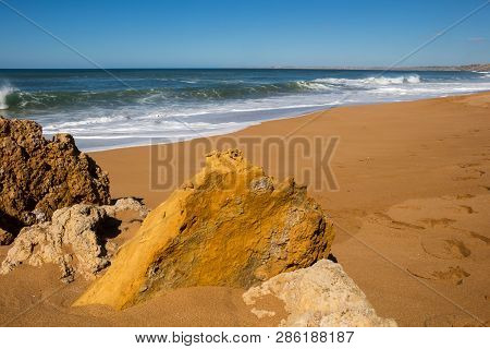 Rocks On The Clean Beach With Dark Yellow Sand. Foamy Waves Of The Atlantic Ocean. Horizon In The Ba