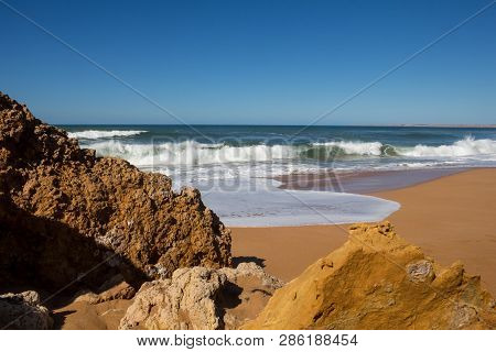 Rocks On The Clean Beach With Dark Yellow Sand. Foamy Waves Of The Atlantic Ocean. Horizon In The Ba