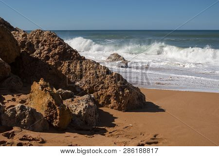 Rocks On The Clean Beach With Dark Yellow Sand. Foamy Waves Of The Atlantic Ocean. Horizon In The Ba