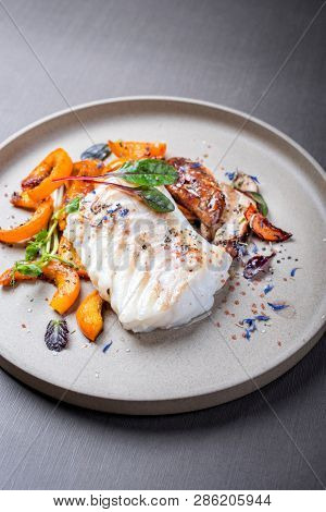 Fried Danish skrei cod fish filet with pumpkin, mushroom and lettuce as closeup on a modern design plate