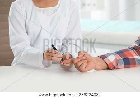 Doctor Taking Patient's Blood Sample With Lancet Pen In Hospital, Closeup. Diabetes Control