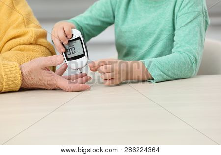 Senior Woman With Her Grandson Using Digital Glucometer At Table, Closeup. Diabetes Control