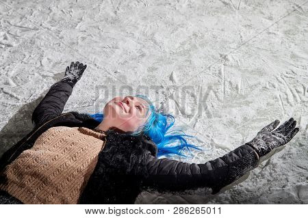 Girl With Blut Hair Lying On The Snow Of A Ice Arena In The Evening City Square In Winter