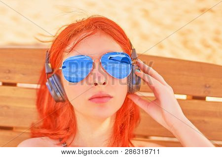 Beautiful Woman Listening To Music On The Beach. Portrait Of A Red-haired Woman In Sunglasses Restin