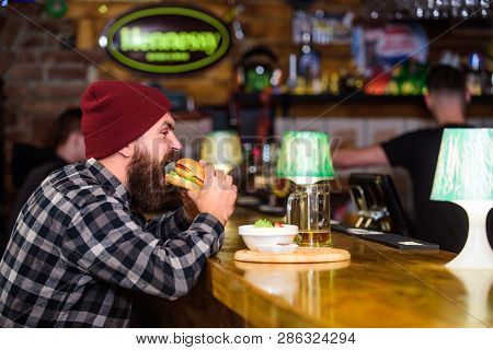 Man With Beard Eat Burger Menu. Brutal Hipster Bearded Man Sit At Bar Counter. High Calorie Food. Ch