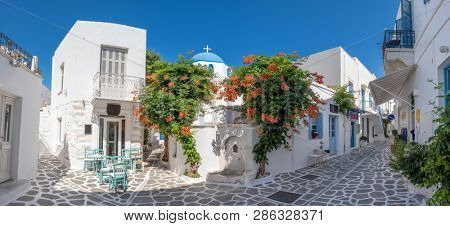 Panorama of the beautiful narrow street in Greece with cozy outdoor cafe and traditional greek church in Parikia town on Paros island, Cyclades