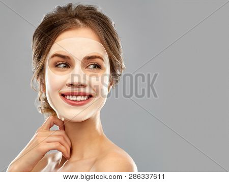 beauty, cosmetology and rejuvenation concept - smiling young woman with hydrogel or sheet facial mask over grey background