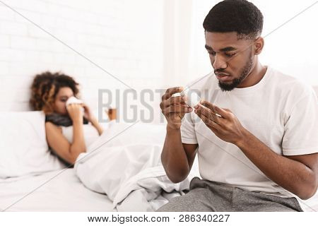 Love And Care. Attentive Man Bringing Medicaments To His Sick Grilfriend Lying In Bed, Reading Instr