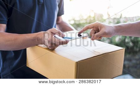 Delivery Mail Man Giving Parcel Box To Recipient, Young Man Appending Signing In Digital Mobile Phon
