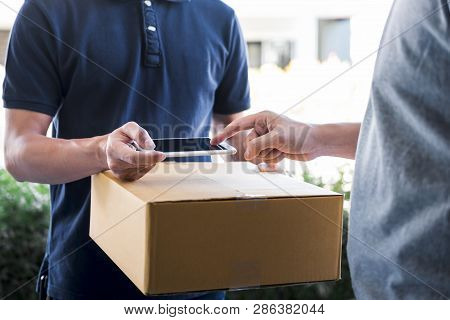 Delivery Mail Man Giving Parcel Box To Recipient, Young Man Appending Signing In Digital Mobile Phon