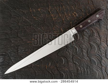 Long chef's knife on black wooden cutting board shot from above